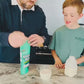 Parent mixing Super Henry chocolate greens into milk with their child.