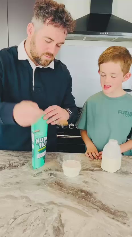 Parent mixing Super Henry chocolate greens into milk with their child.